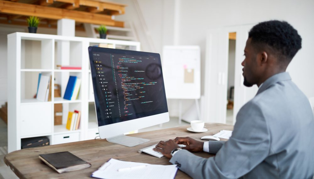 Work of it-developer Young elegant software developer in formalwear sitting by desk in front of computer screen while decoding data